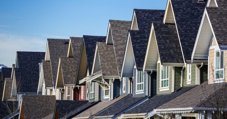 Side profile photo of 8 Townhouses roofs in a row, ona clear day.