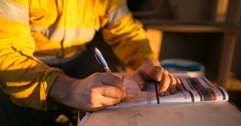 Man in a yellow reflective utility jacket, filling out a form