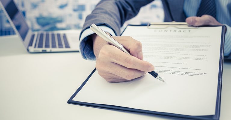 Person's hand pointing with a pen to a clipboard asking for a signature