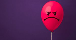 Photo of a red Balloon with an angry face drawn on it, in front of a purple background