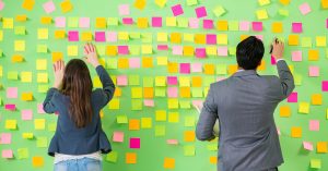 Man and Woman in front of a wall filled with post it notes.