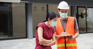 City worker in safety gear explaining something on a sheet of paper to a woman in ppe mask.